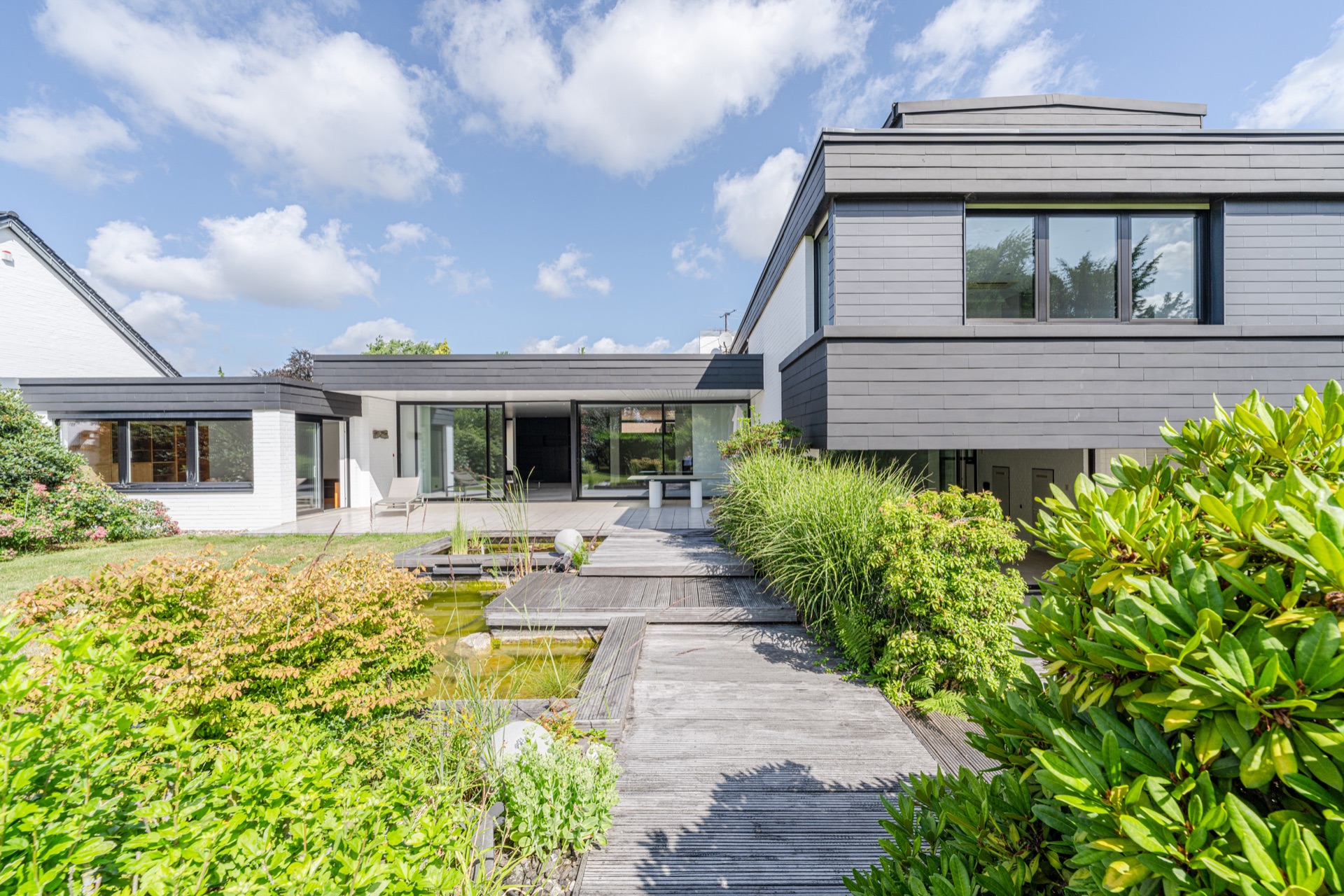 Moderner Wohnhaus-Garten mit Holzsteg, Teich und großen Fenstern.