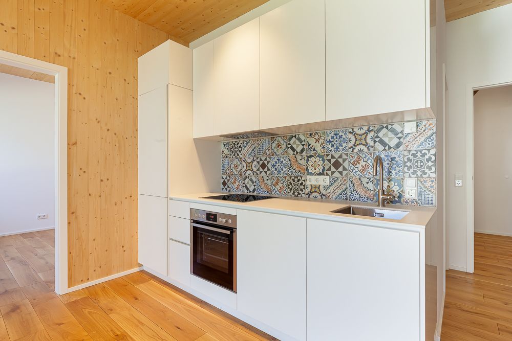 Moderne weiße Küchenzeile mit gemusterten Fliesen und Holzverkleidung an Wand und Boden.