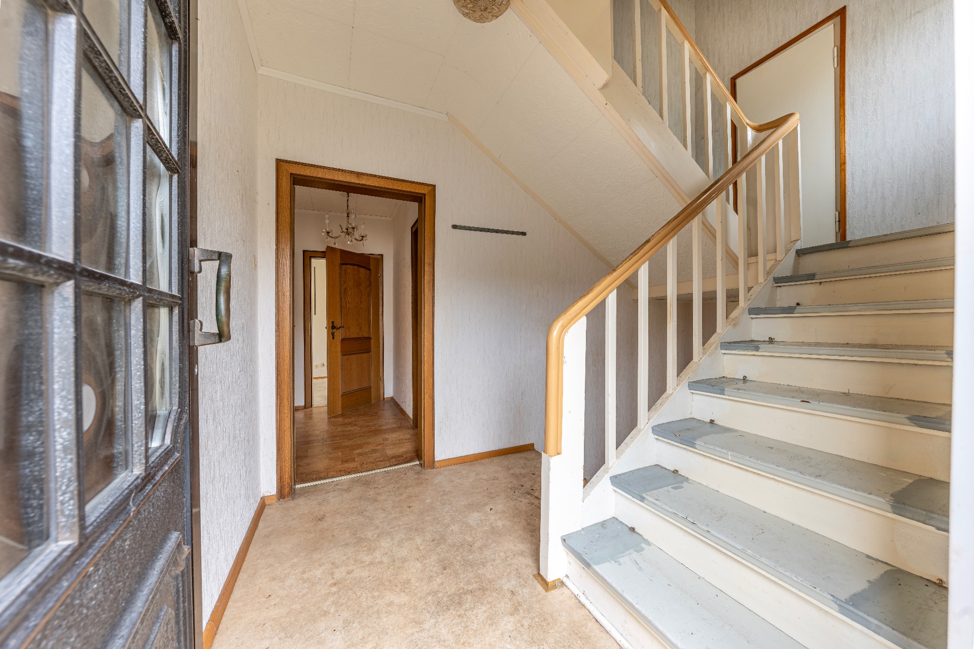 Flur mit Treppe, Holzgeländer und offenem Durchgang zu weiteren Räumen in einem Wohnhaus.