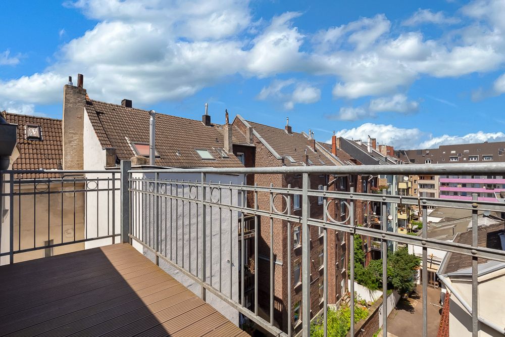 Balkon mit Metallgeländer, Blick auf Nachbarhäuser und blauen Himmel mit Wolken.