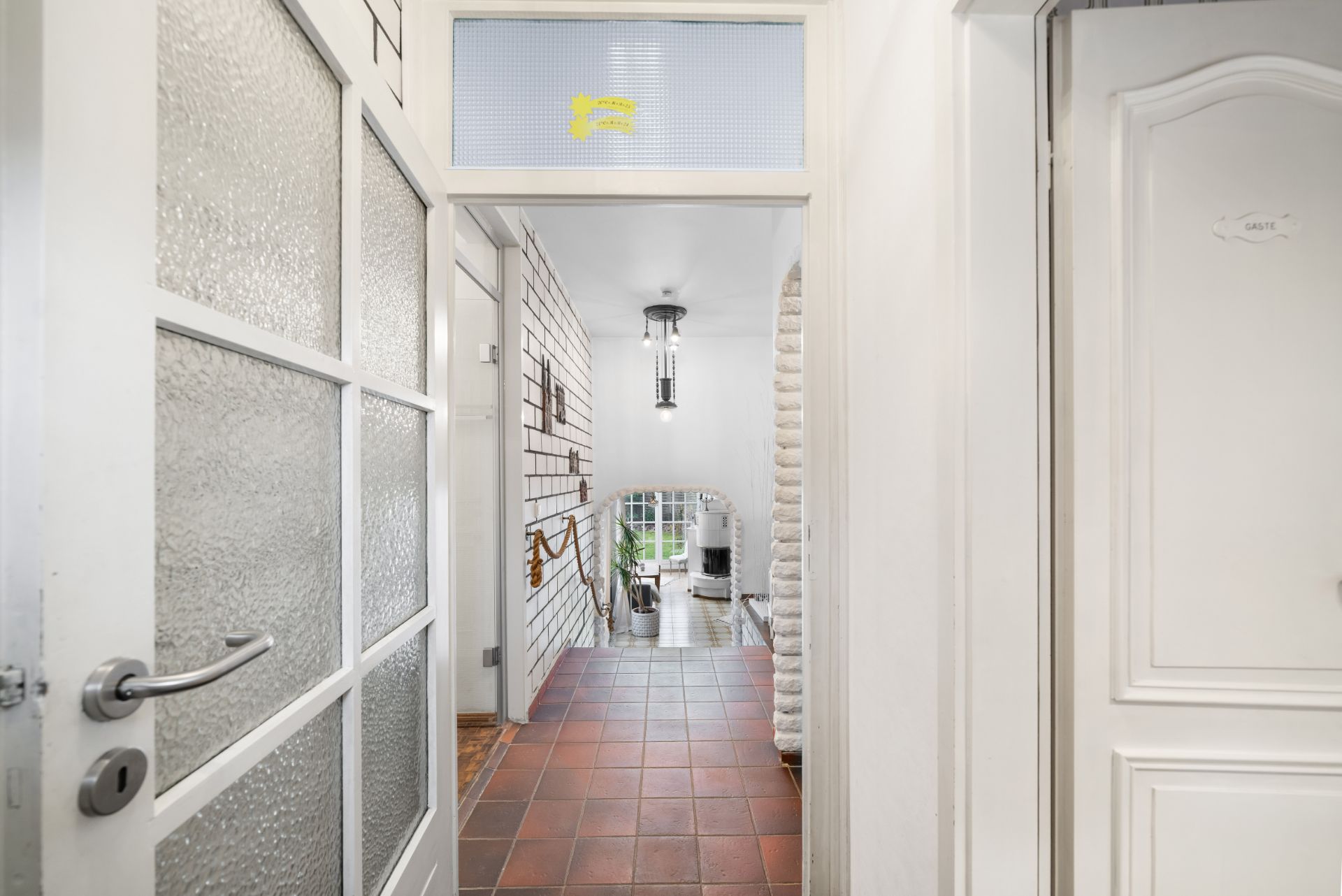 Heller Flur mit roten Bodenfliesen, weißen Türen und Zugang zu einer Treppe.