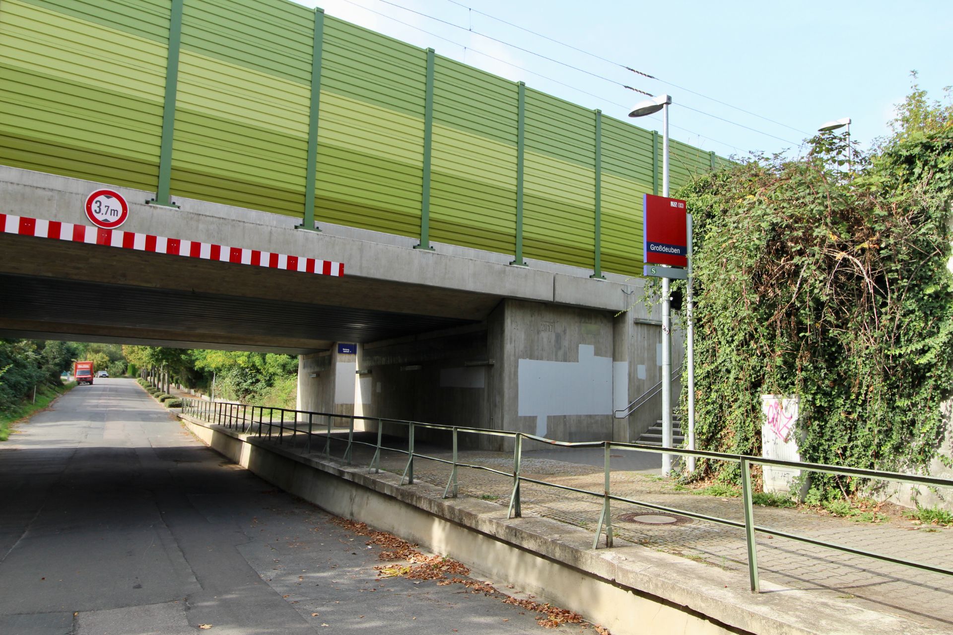 Fußgängerunterführung unter einer Brücke mit grünem Lärmschutz und Geländer.