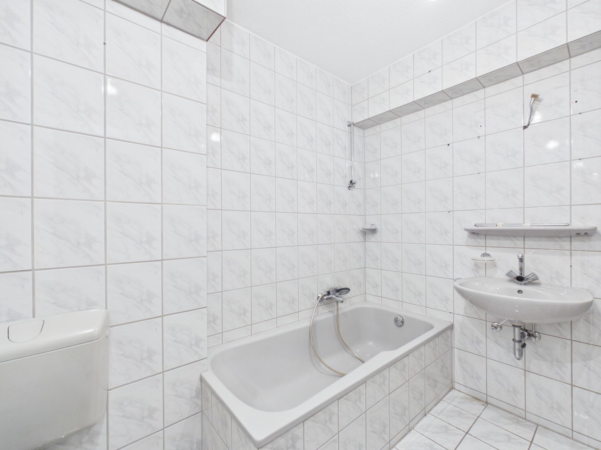 Helles Badezimmer mit Badewanne, Waschbecken und weißen Fliesen an Wänden und Boden.