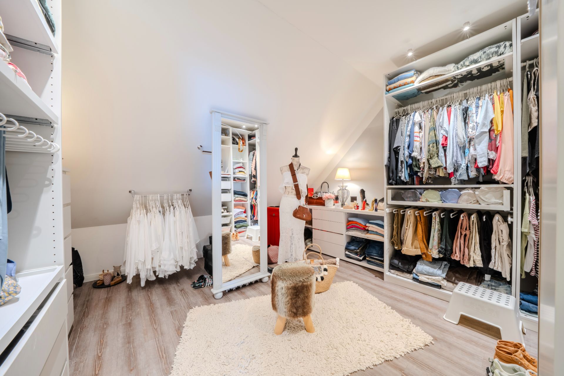 Geräumiges Ankleidezimmer mit Kleiderschränken, Spiegel, Teppich und Hocker auf Holzfußboden.