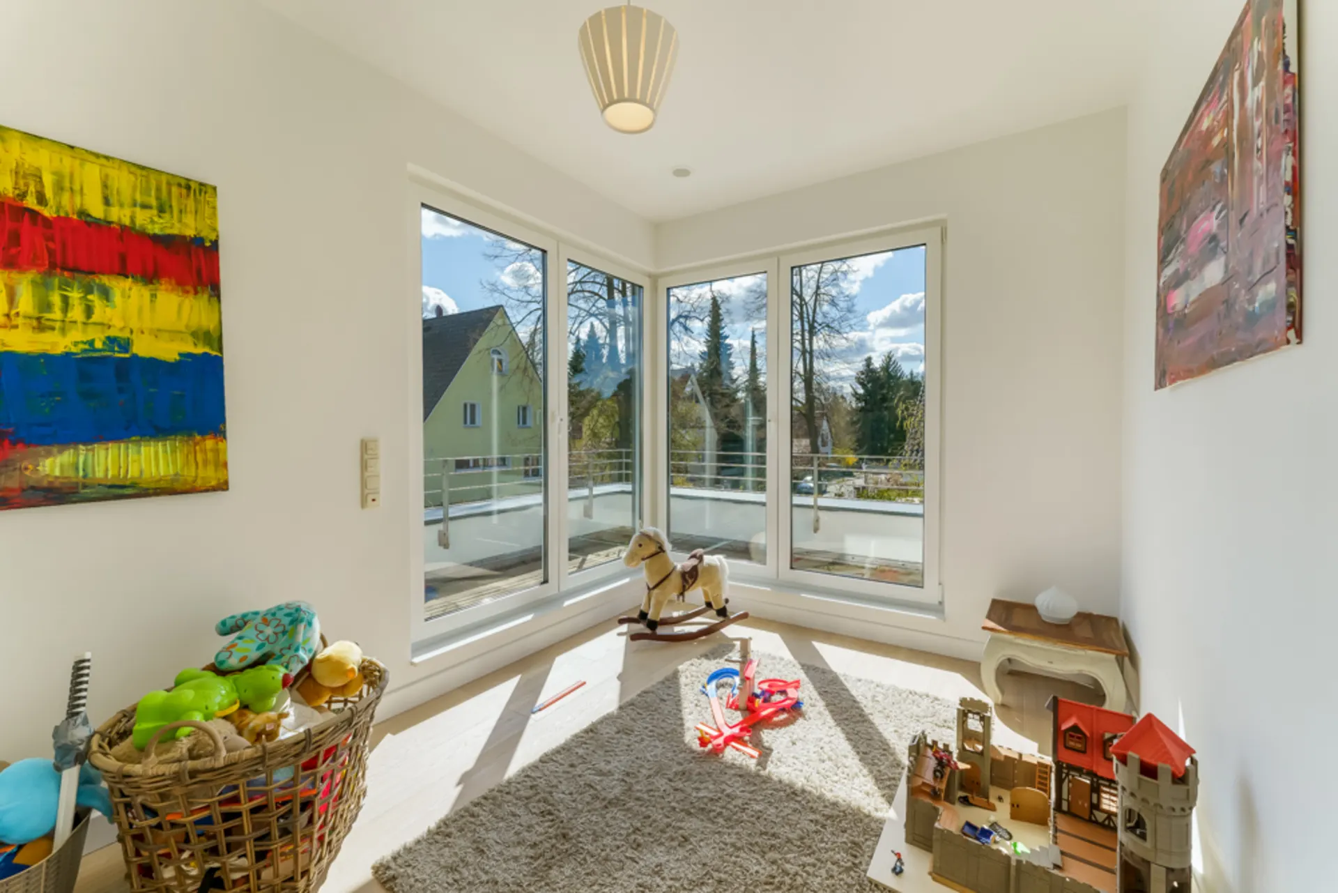 Helles Kinderzimmer mit Spielzeug, großem Fenster und bunter Wandkunst.