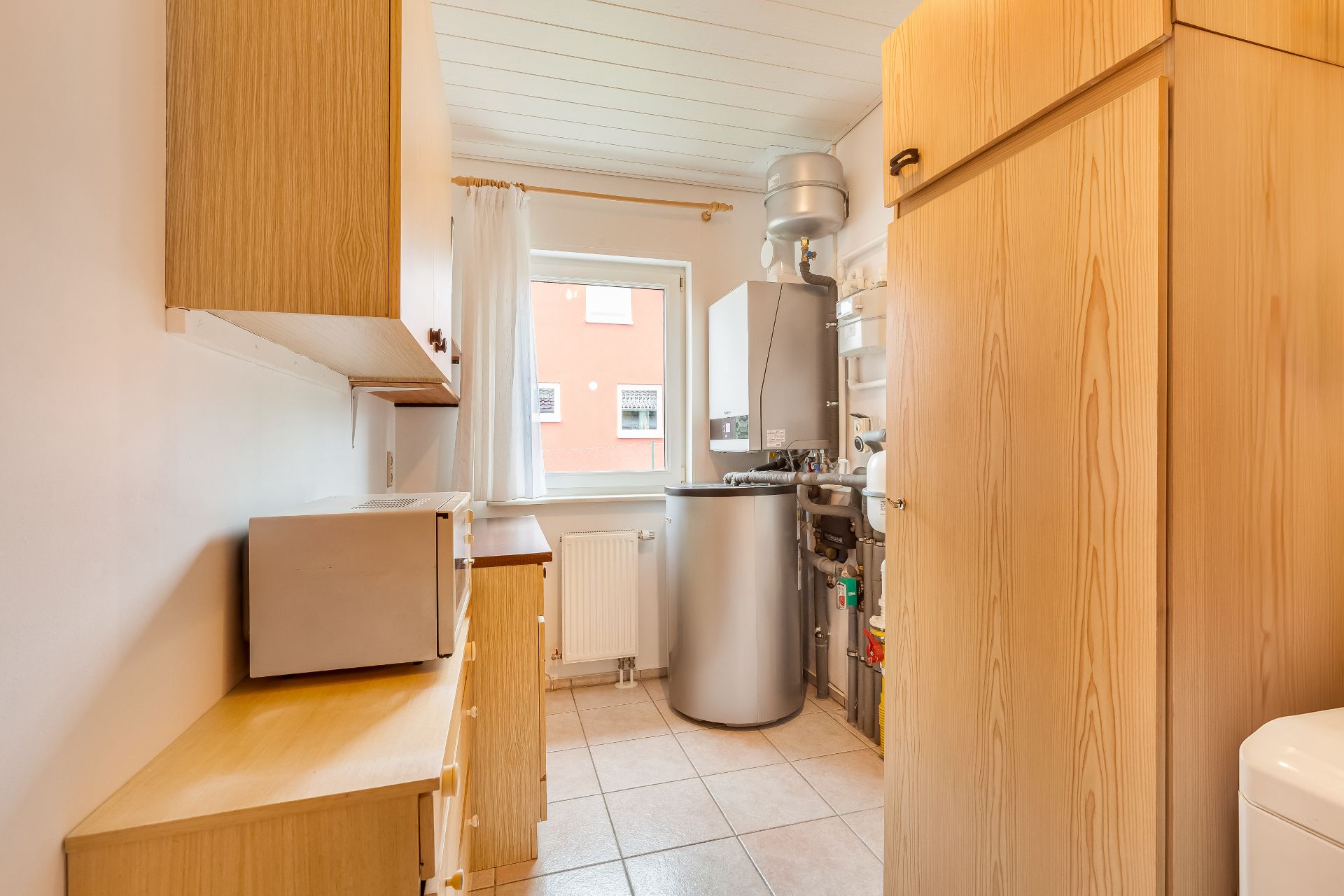Hauswirtschaftsraum mit Holzschränken, Mikrowelle, Heizungsanlage und Fenster.