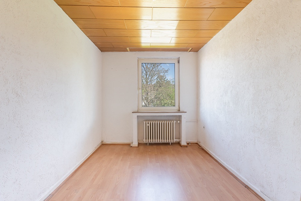 Leeres Zimmer mit Holzdecke, Fenster, Heizkörper und hellem Laminatboden.