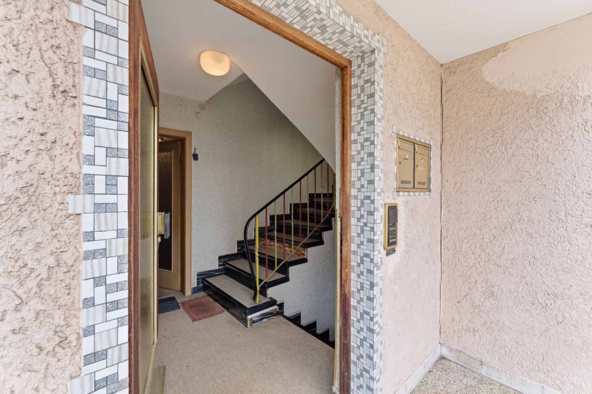 Eingangsbereich eines Wohnhauses mit Tür, Treppenhaus und Briefkästen an der Wand.