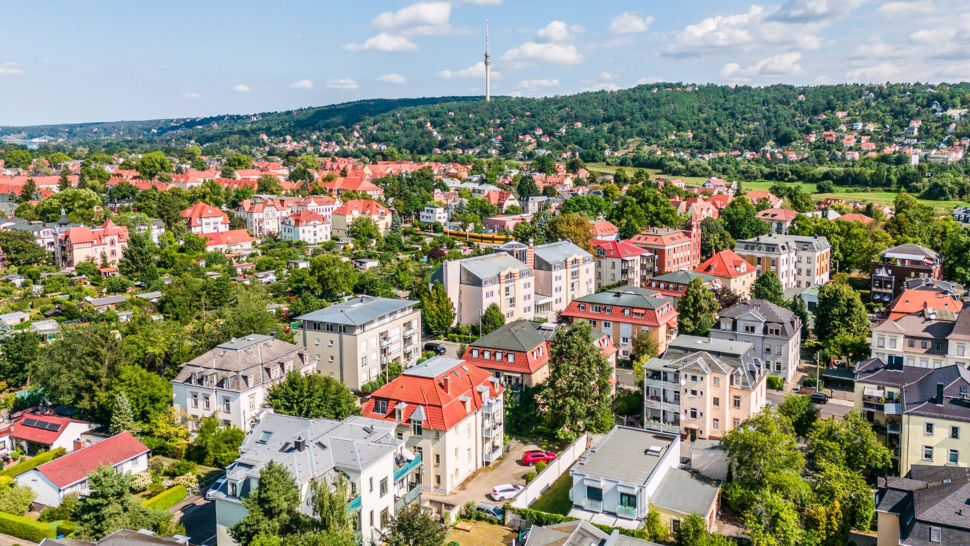Luftaufnahme eines Wohngebiets mit mehreren Häusern, viel Grün und einem Hügel im Hintergrund.