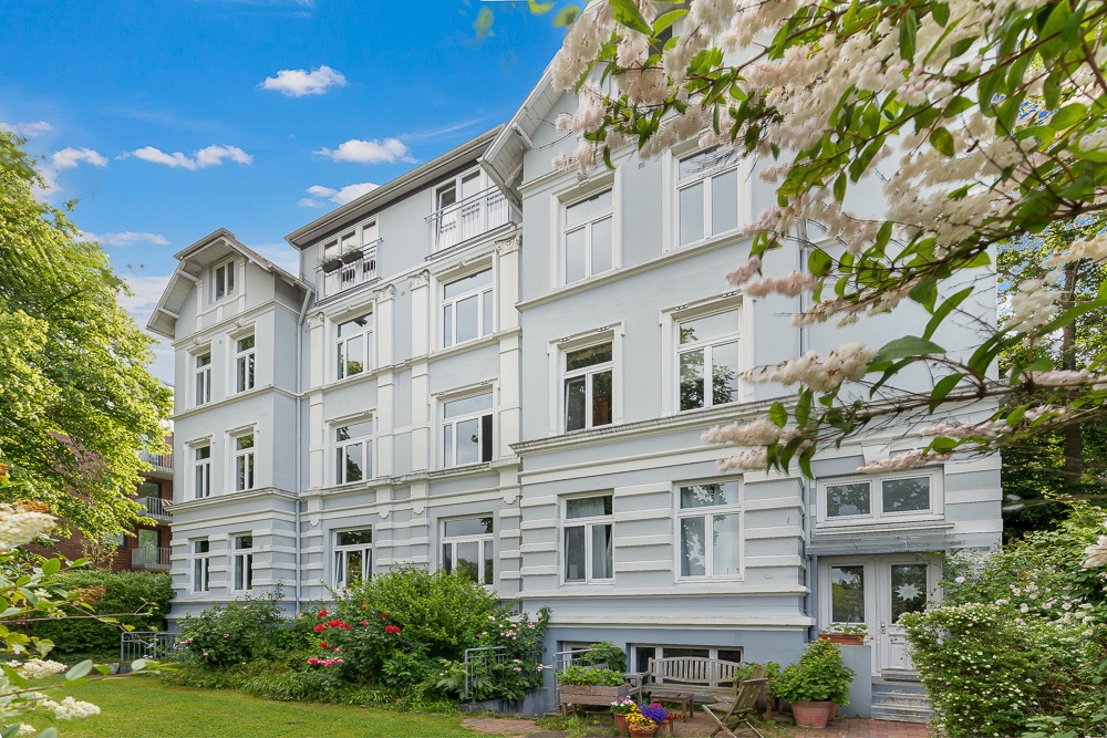 Helles, mehrstöckiges Wohngebäude mit weißen Fassaden und Garten im Vordergrund.