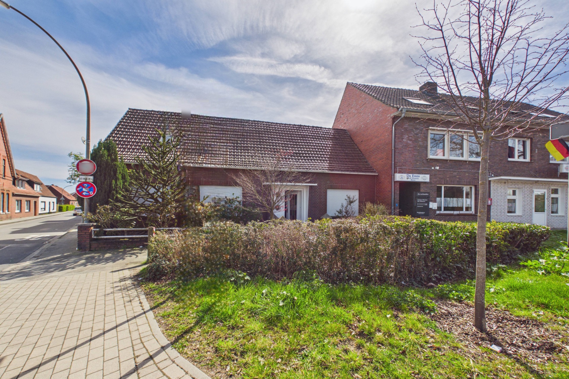 Vorderansicht eines Hauses mit Vorgarten, Gehweg und angrenzender Straße bei Tageslicht.