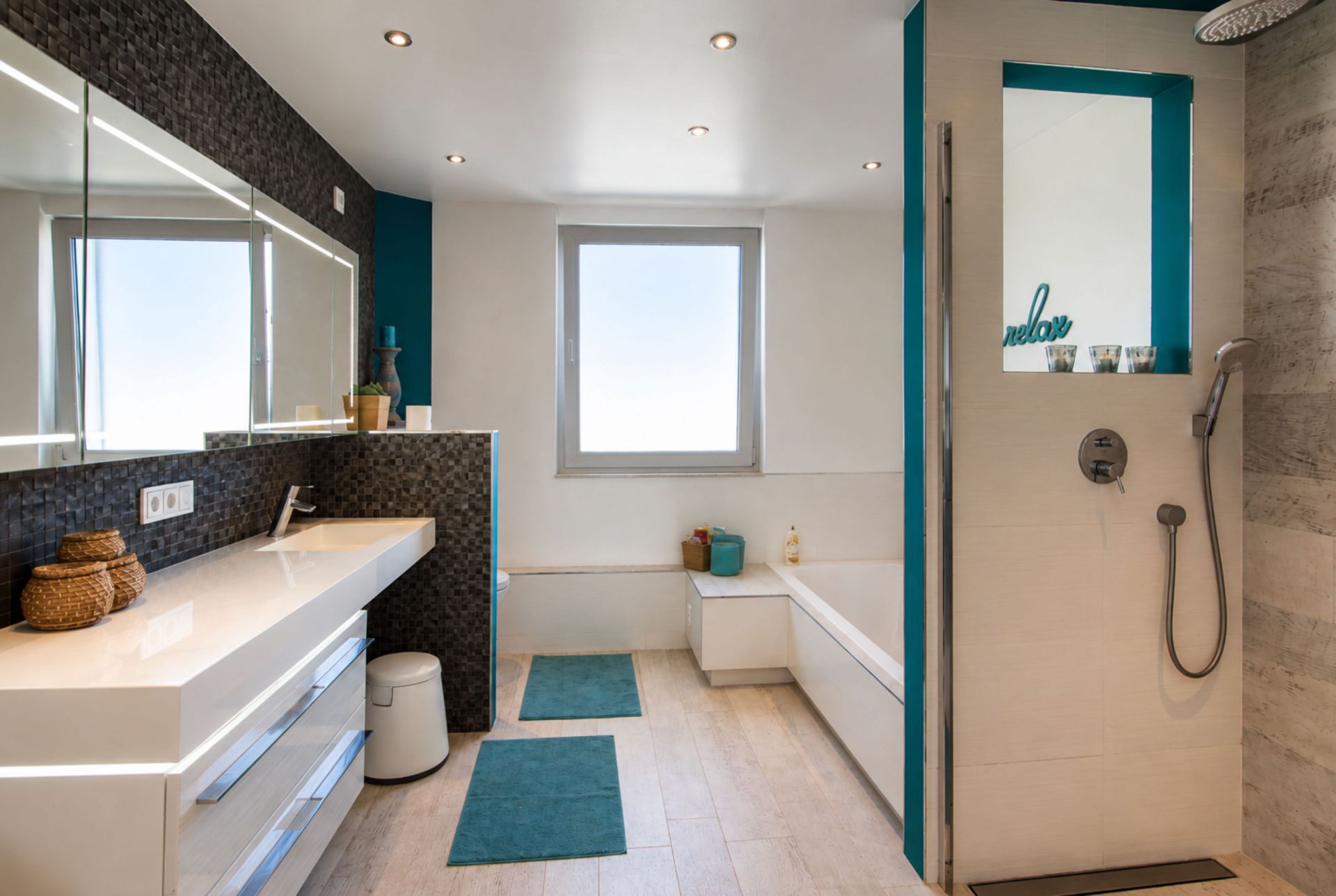 Modernes Badezimmer mit großer Dusche, Badewanne, weißem Waschbecken und Spiegel, zwei Teppichen auf dem Boden.