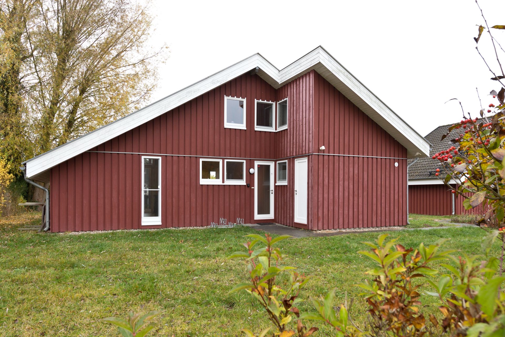 Rotes Holzhaus mit weißem Dach, mehreren Fenstern und einer Tür, umgeben von Rasen.