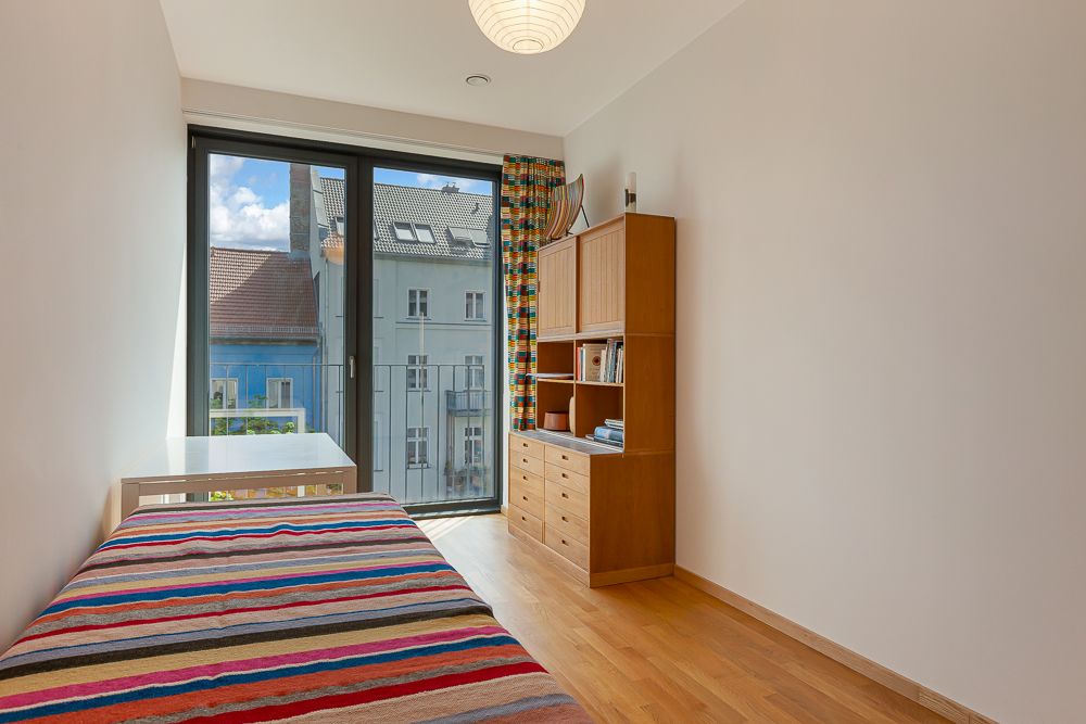 Helles Schlafzimmer mit Einzelbett, Holzregal und großem Fenster mit Blick auf Nachbarhäuser.