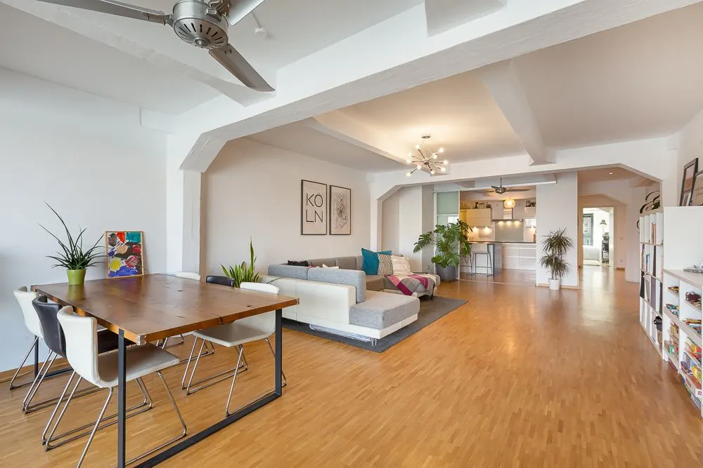 Offener Wohnbereich mit Holzboden, Essbereich, Sofa, Pflanzen und moderner Küche im Hintergrund.