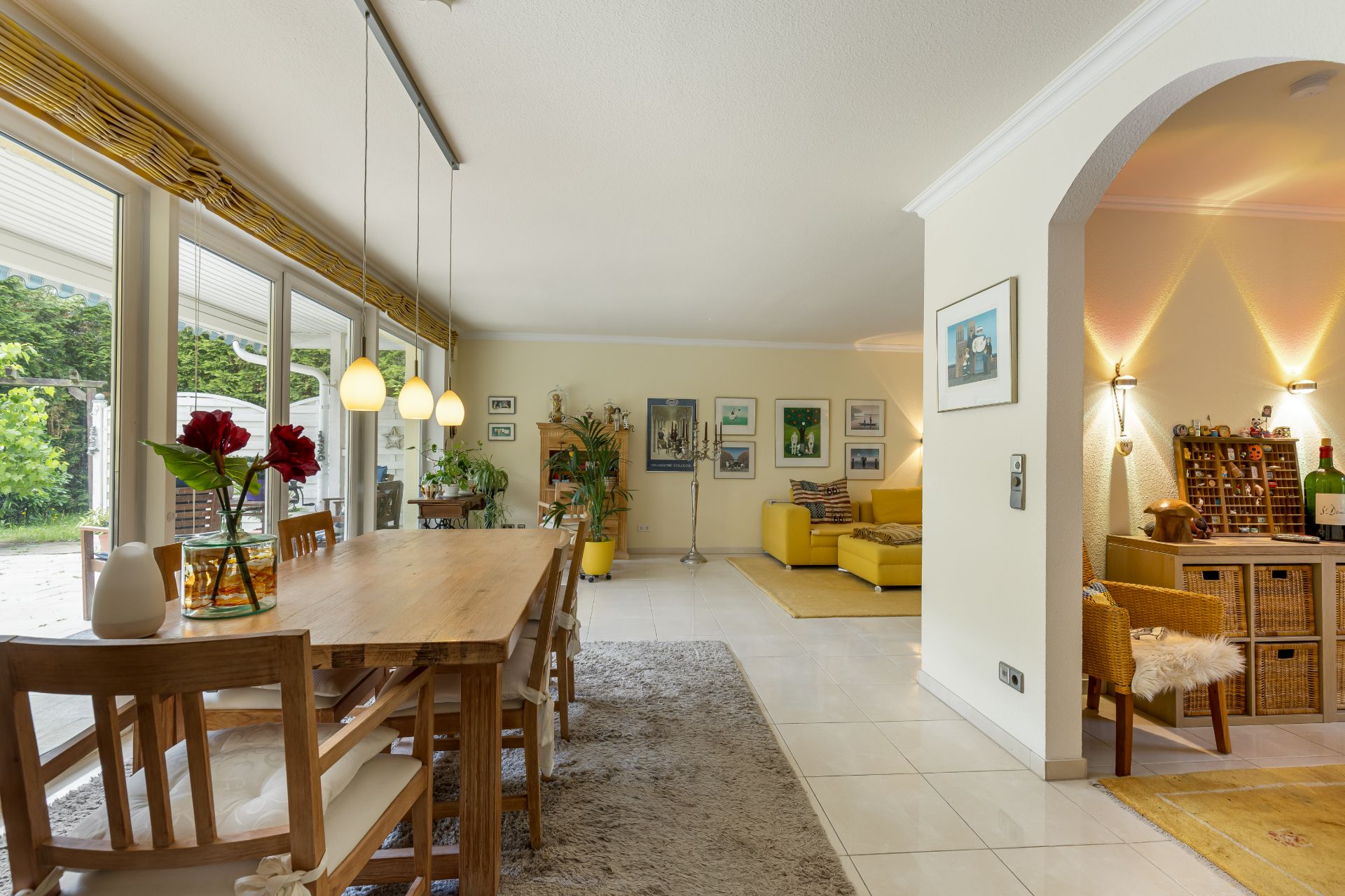 Helles Wohnzimmer mit Esstisch, gelbem Sofa und großen Fenstern mit Blick auf den Garten.