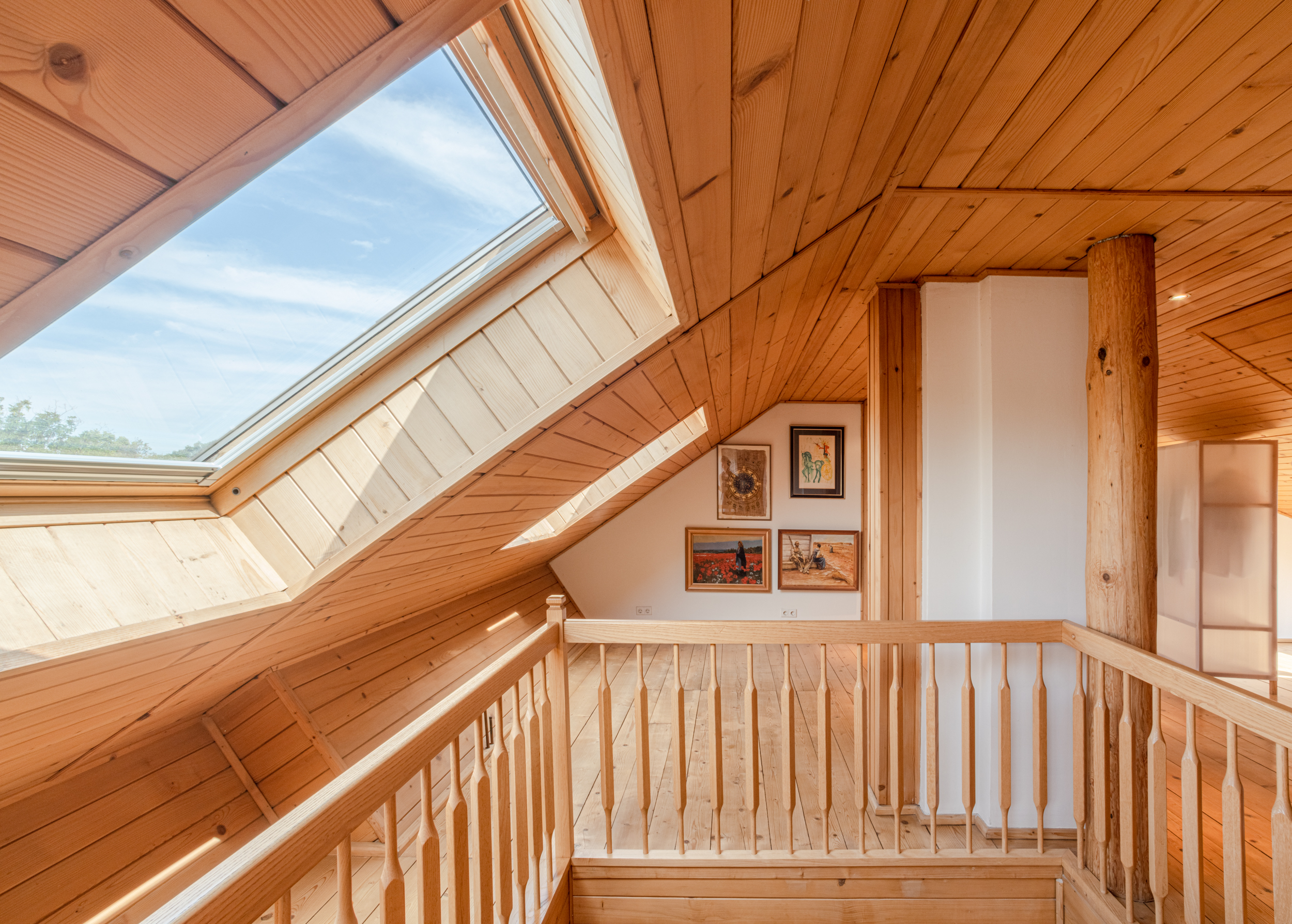 Dachgeschoss mit Holzverkleidung, großem Dachfenster und Bildern an der Wand.