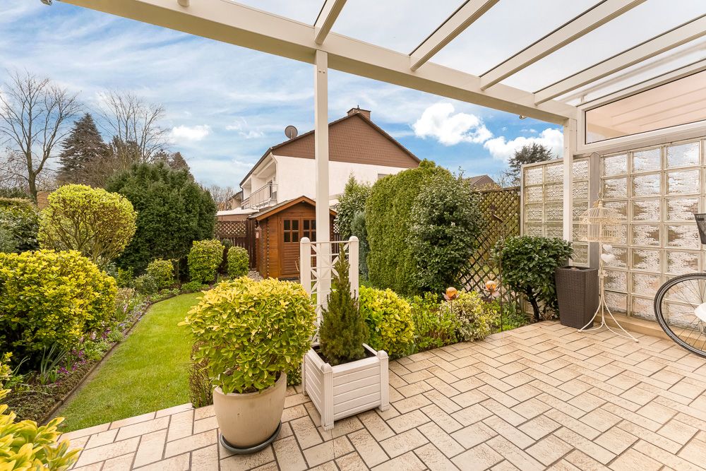 Überdachte Terrasse mit Fliesenboden und Blick auf einen gepflegten Garten mit Gartenhaus.