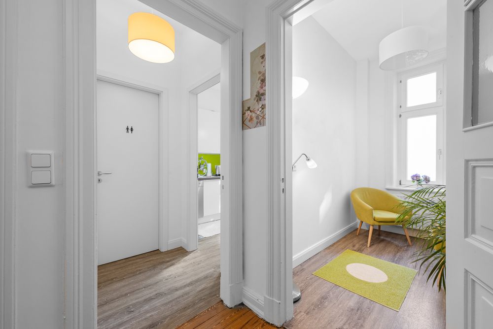 Heller Flur mit Zugang zu einem Raum mit gelbem Sessel, Lampe und grünem Teppich.