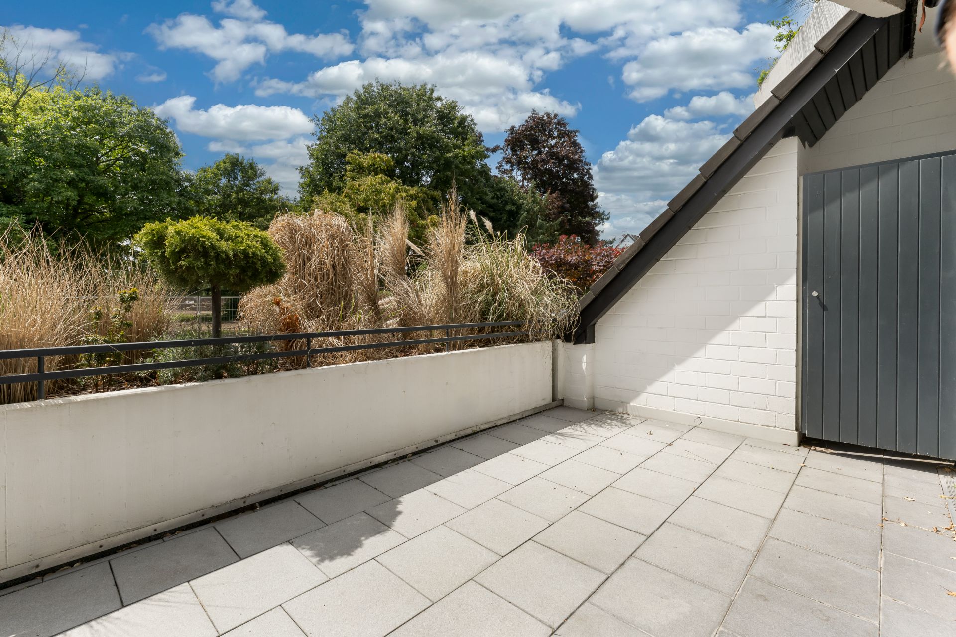 Geräumige Terrasse mit Steinboden, Pflanzen an der Brüstung und Blick auf Bäume.
