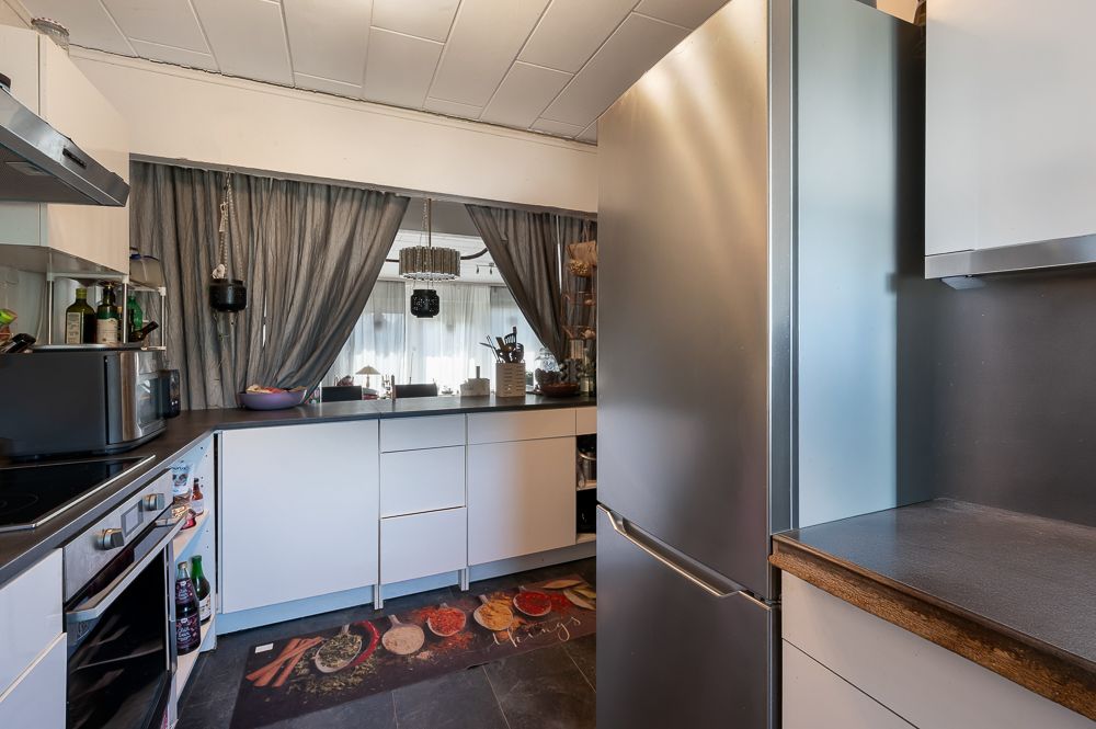 Moderne Küche mit weißen Schränken, großem Kühlschrank und grauen Vorhängen am Fenster.