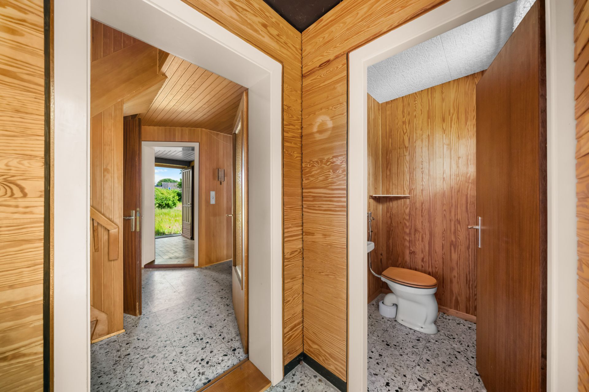 Flur mit Blick auf ein WC und eine Treppe, Wände und Türen aus Holz.