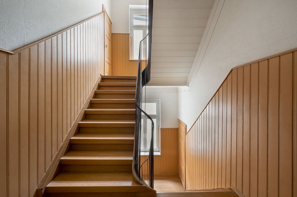 Holztreppe mit brauner Wandverkleidung und Handlauf in einem Wohnhausflur.