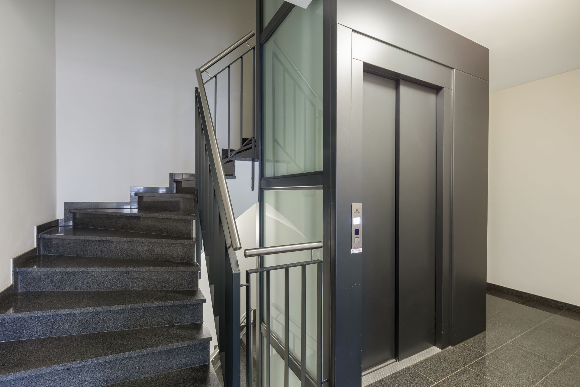 Treppe und Aufzug in einem modernen Wohngebäude mit grauen Fliesen.