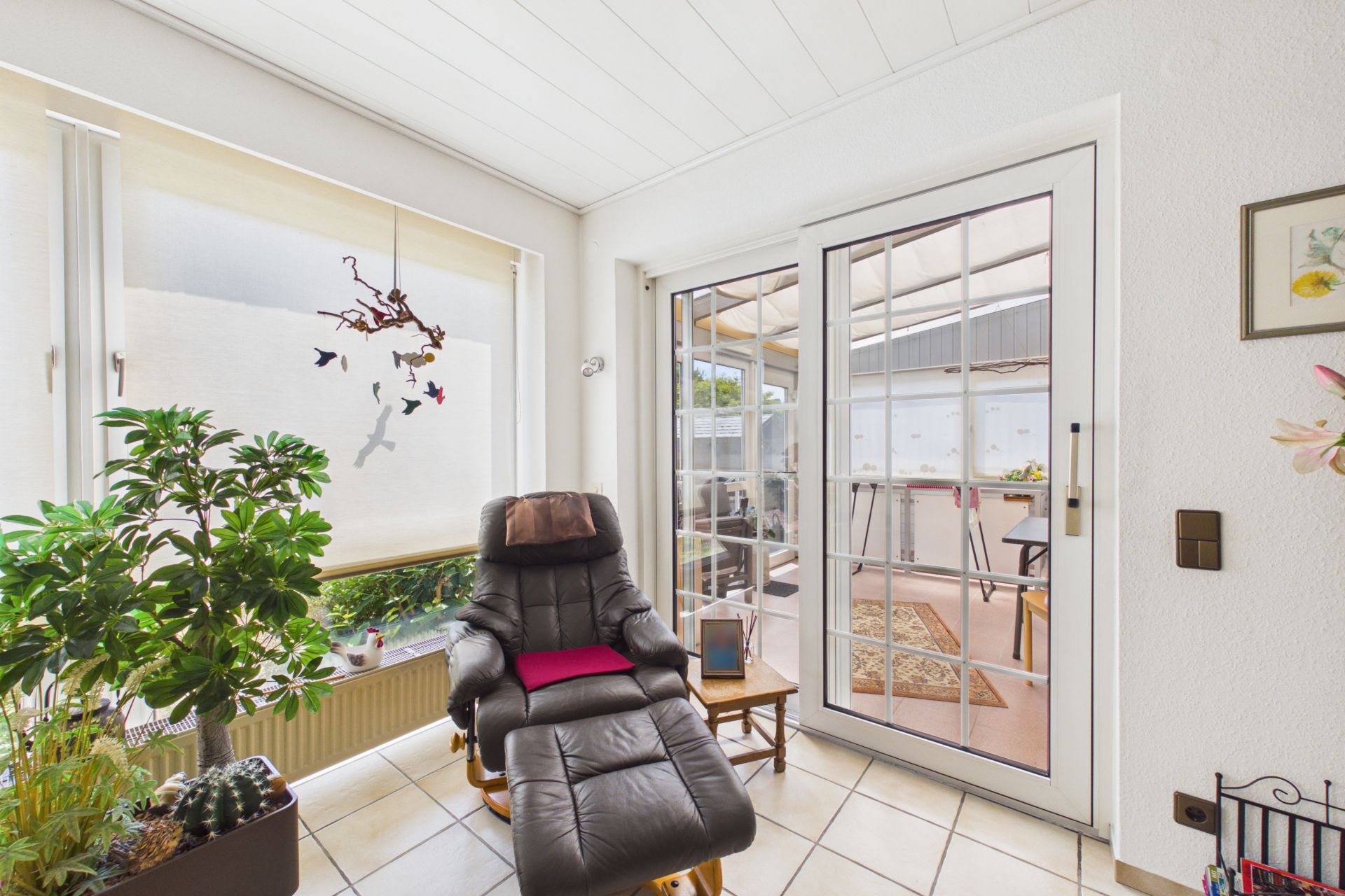 Heller Raum mit Sessel, Beistelltisch, Pflanzen und Glastür zur Terrasse.