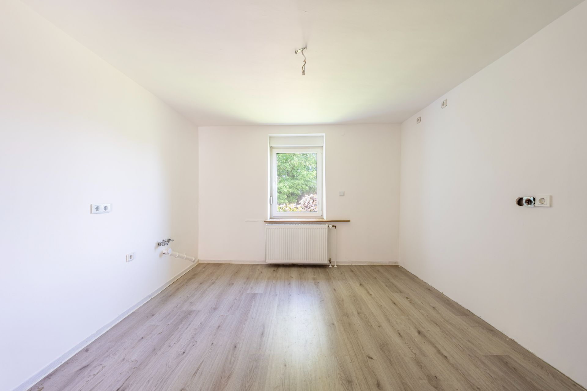 Leerer heller Raum mit Holzboden und einem Fenster an der Stirnwand.