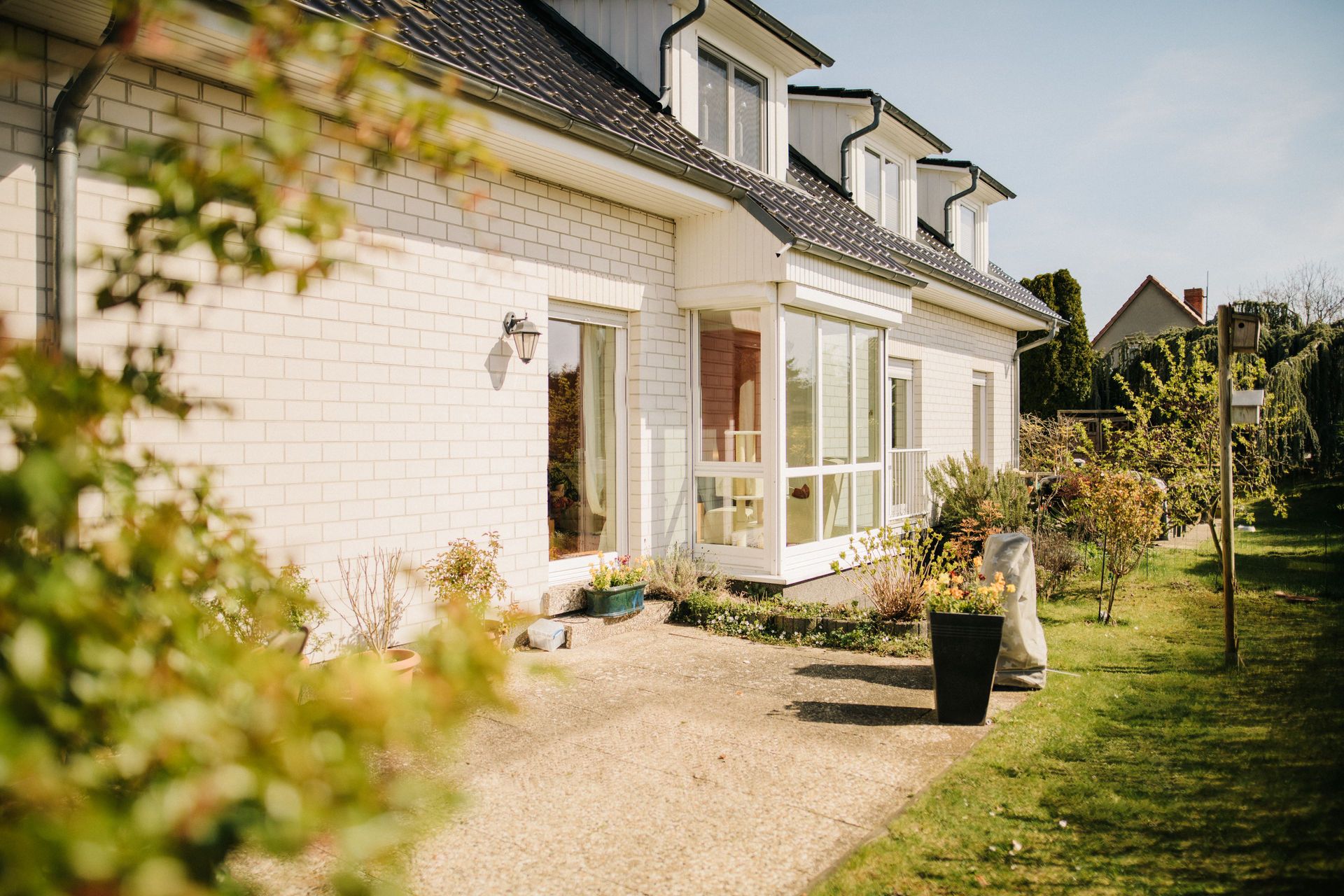Modernes Wohnhaus mit Terrasse, großen Fenstern und Garten im Sonnenschein.