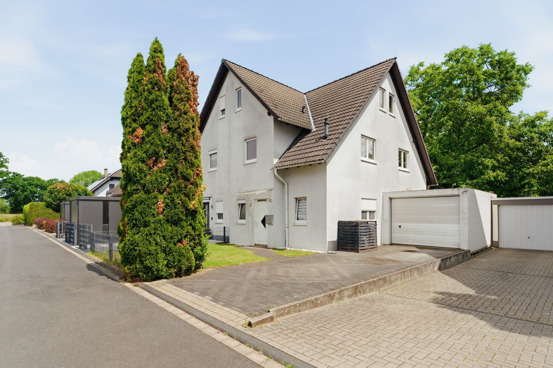 Modernes Einfamilienhaus mit grauem Dach, Garage und gepflasterter Einfahrt an einer ruhigen Straße.