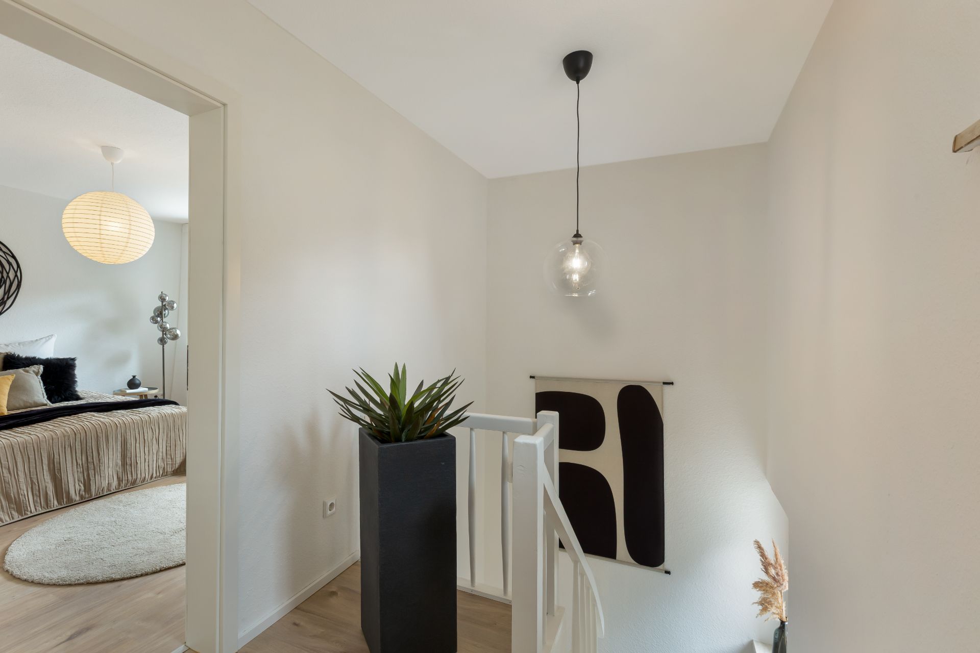 Heller Flur mit Treppe, Pflanze, Wandbild und Blick in ein Schlafzimmer.