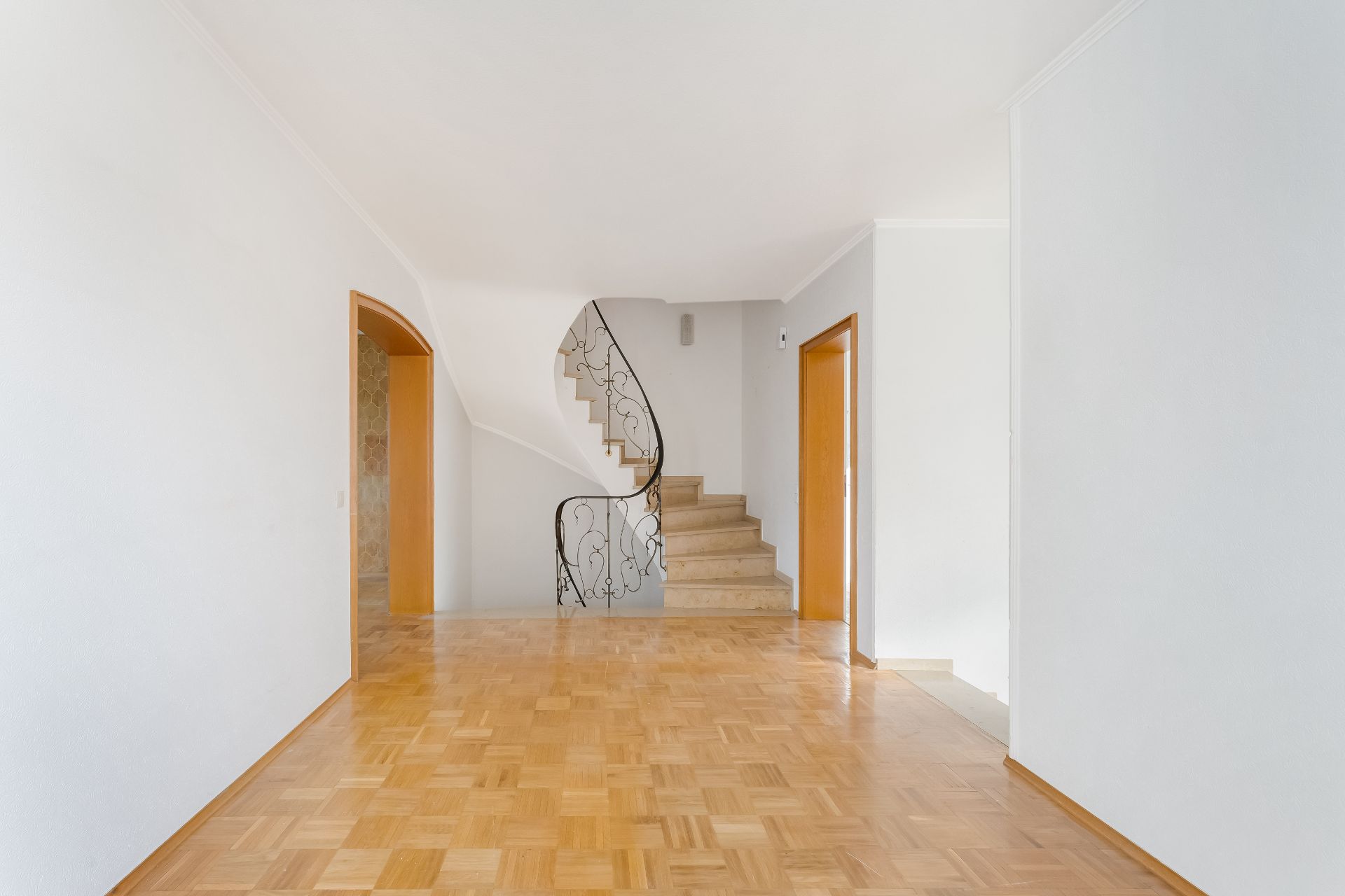 Leerer Raum mit Parkettboden und einer Treppe mit verziertem Geländer.