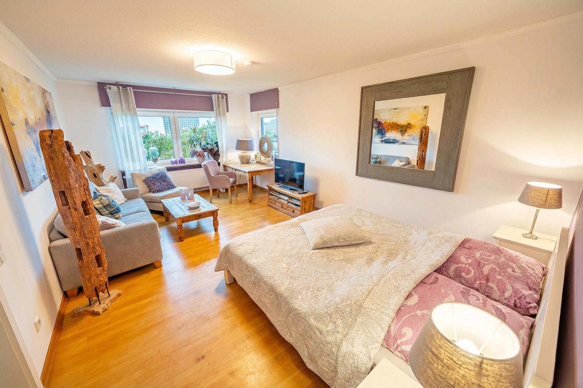 Helles Schlafzimmer mit Doppelbett, Sofa, Fernseher und großem Fenster, Holzboden.