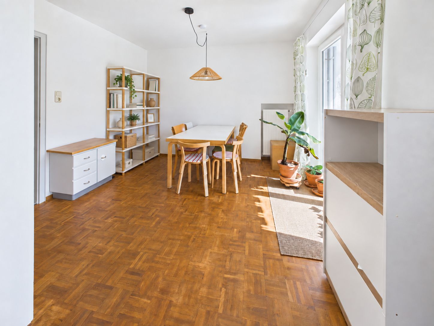 Heller Essbereich mit Holztisch, vier Stühlen, Regal, Zimmerpflanzen und Parkettboden.