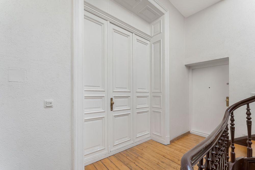 Heller Hausflur mit großer weißer Holztür, Holzboden und Treppengeländer.