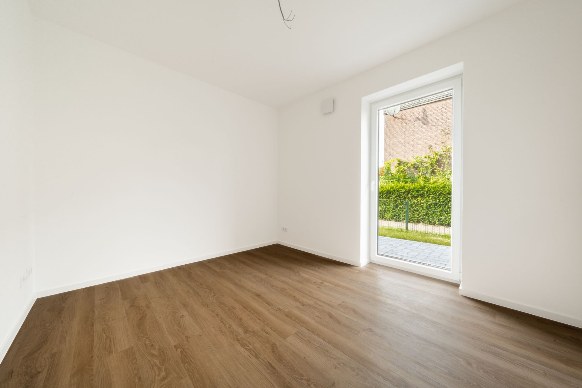Leerer Raum mit Holzfußboden und großem Fenster zum Garten.