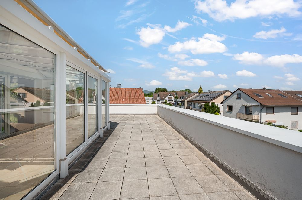 Große Dachterrasse mit Fliesenboden und Glasfront, Blick auf umliegende Wohnhäuser.