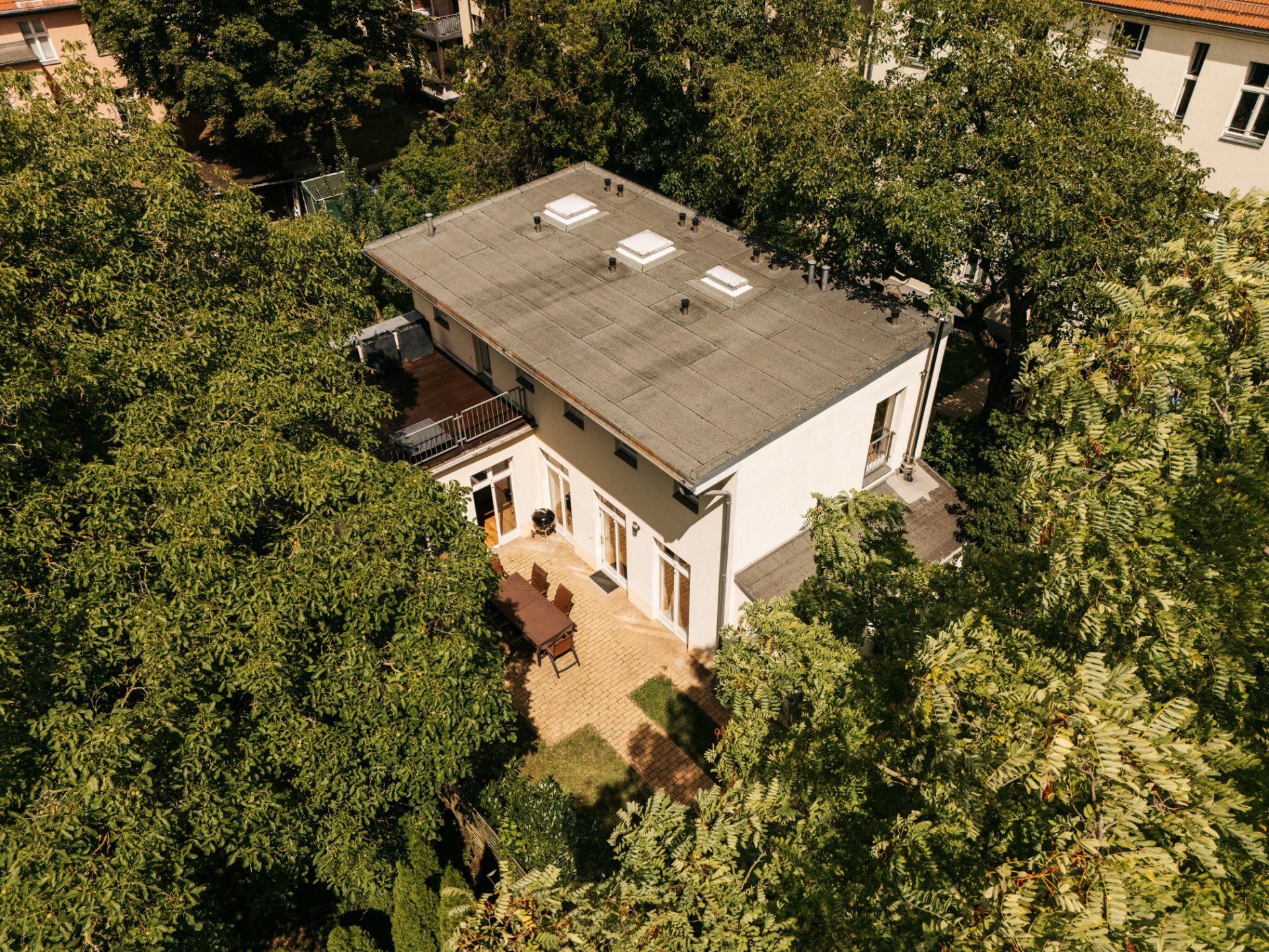 Modernes zweistöckiges Haus mit Flachdach und Terrasse, umgeben von Bäumen.