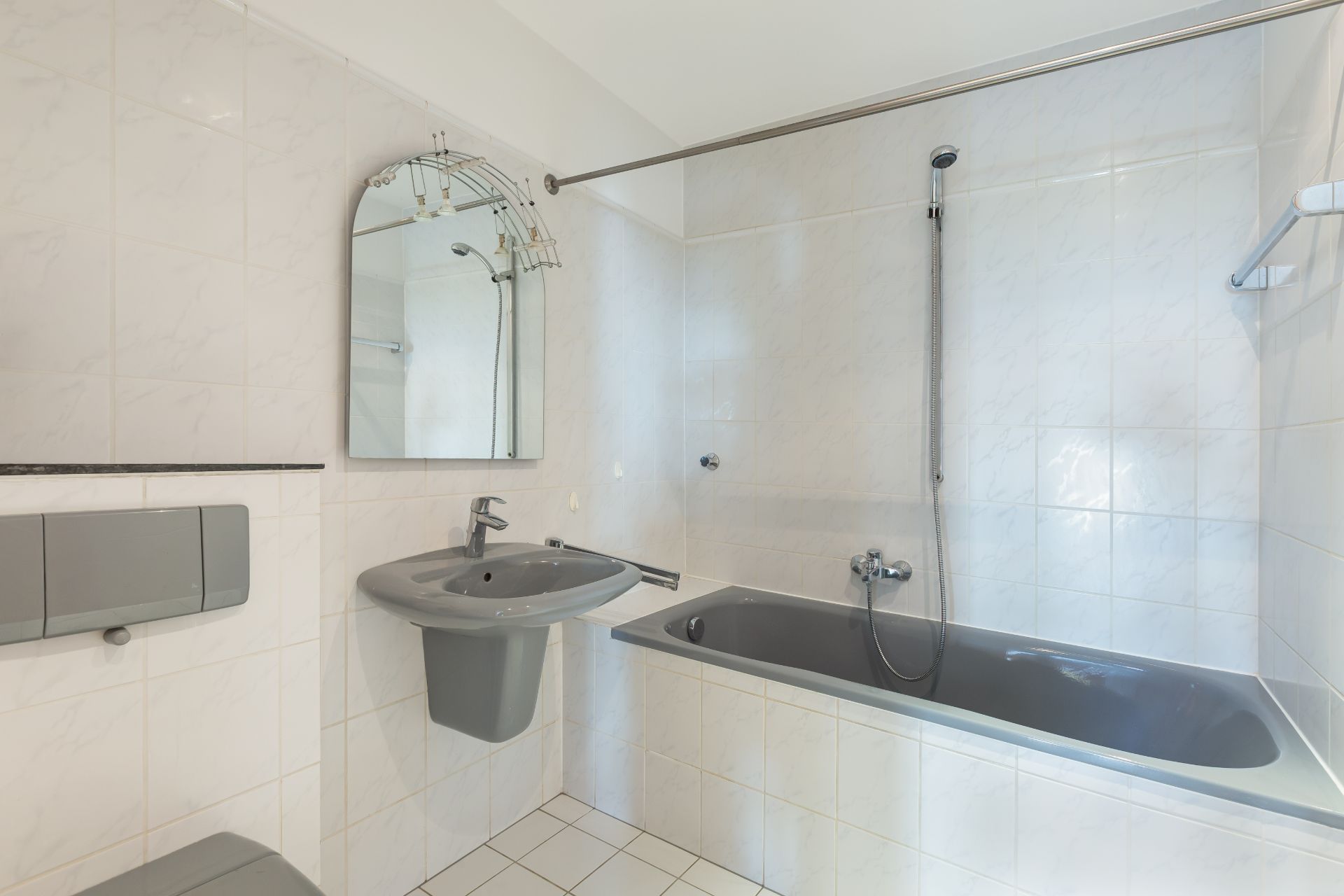 Helles Badezimmer mit grauer Badewanne, Waschbecken, Spiegel und WC.