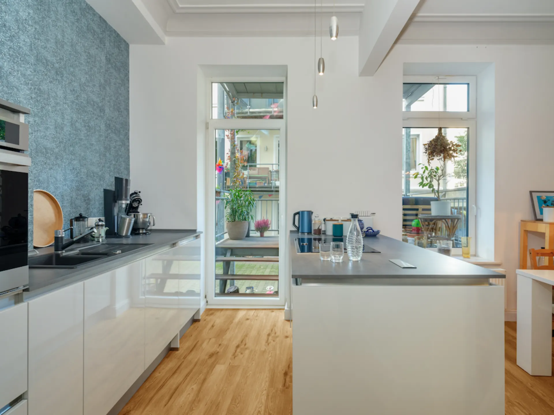 Moderne Küche mit Kücheninsel, Holzfußboden und großen Fenstern mit Blick auf einen Balkon.