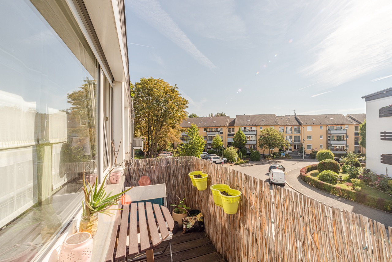 Kleiner Balkon mit Tisch und Pflanzen, Blick auf Wohngebäude und begrünten Hof.
