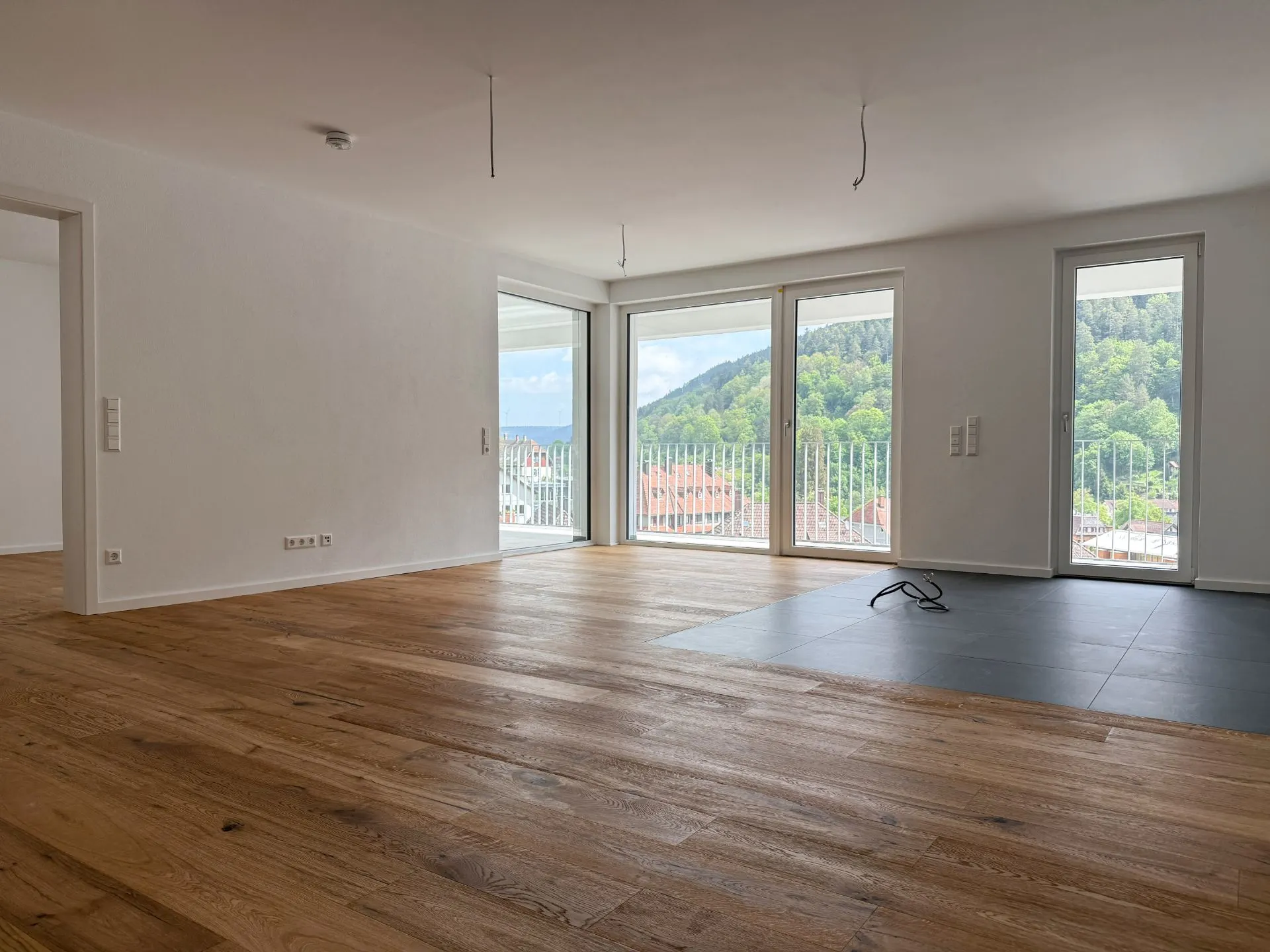 Helles Wohnzimmer mit Holzboden, großen Fenstern und Blick auf grüne Hügel.