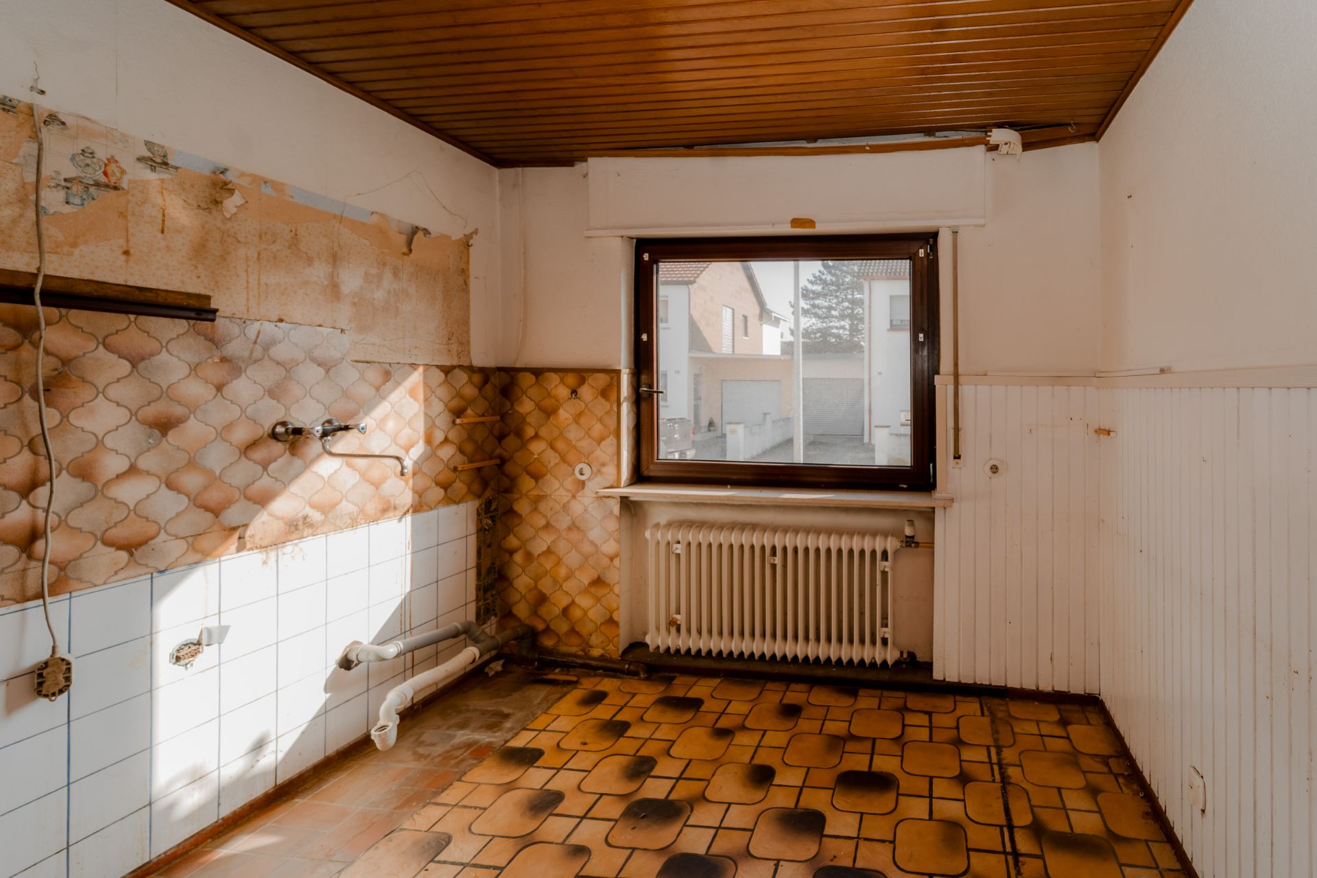 Leerer Raum mit Fliesenboden, Heizkörper unter Fenster und gefliester Wand.