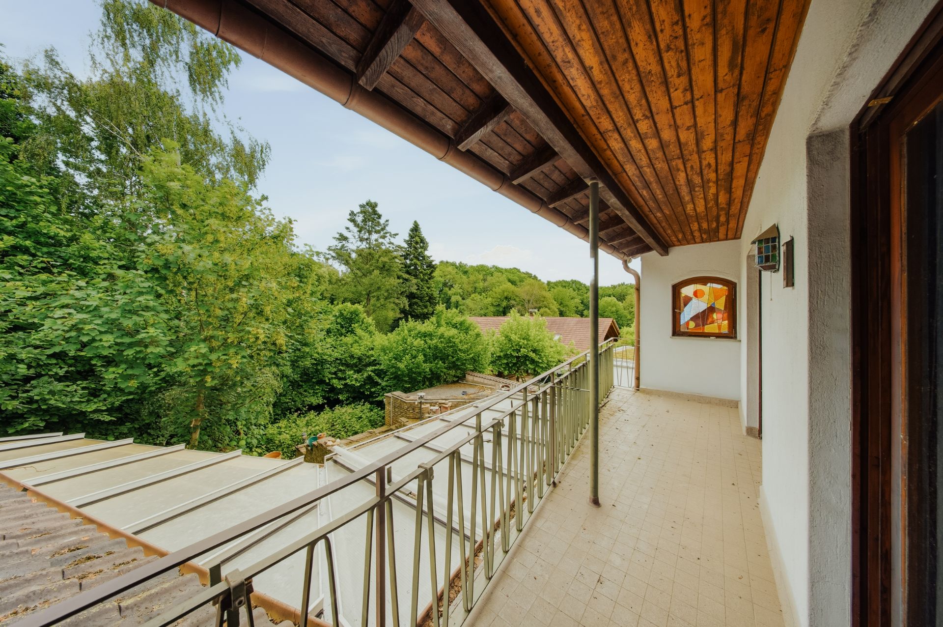 Langer Balkon mit Holzgeländer und Blick auf grüne Bäume im Garten.
