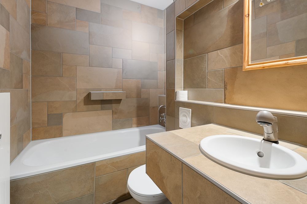 Modernes Badezimmer mit Badewanne, Waschbecken, Spiegel und braunen Fliesen an den Wänden.