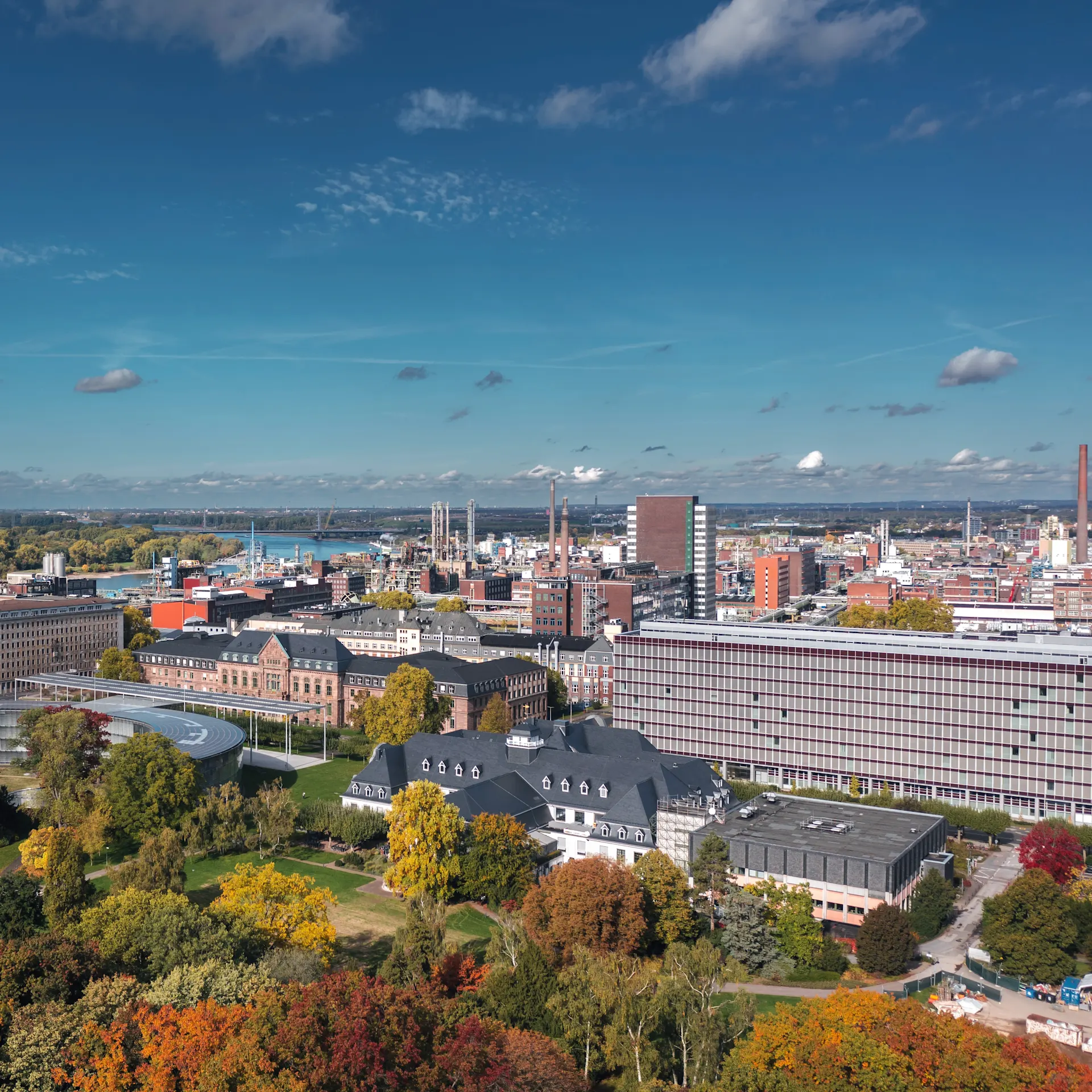 Stadtansicht mit Grünflächen, modernen und historischen Gebäuden unter blauem Himmel.