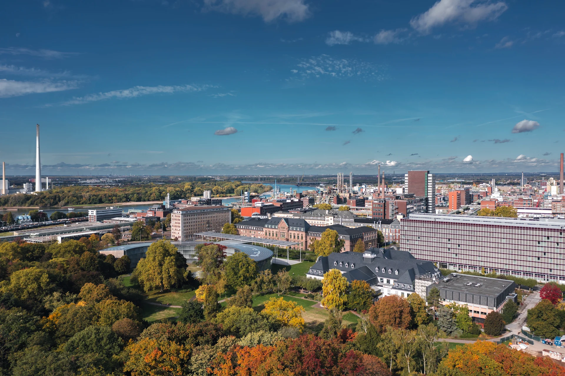 Stadtansicht mit Grünflächen, modernen und historischen Gebäuden unter blauem Himmel.