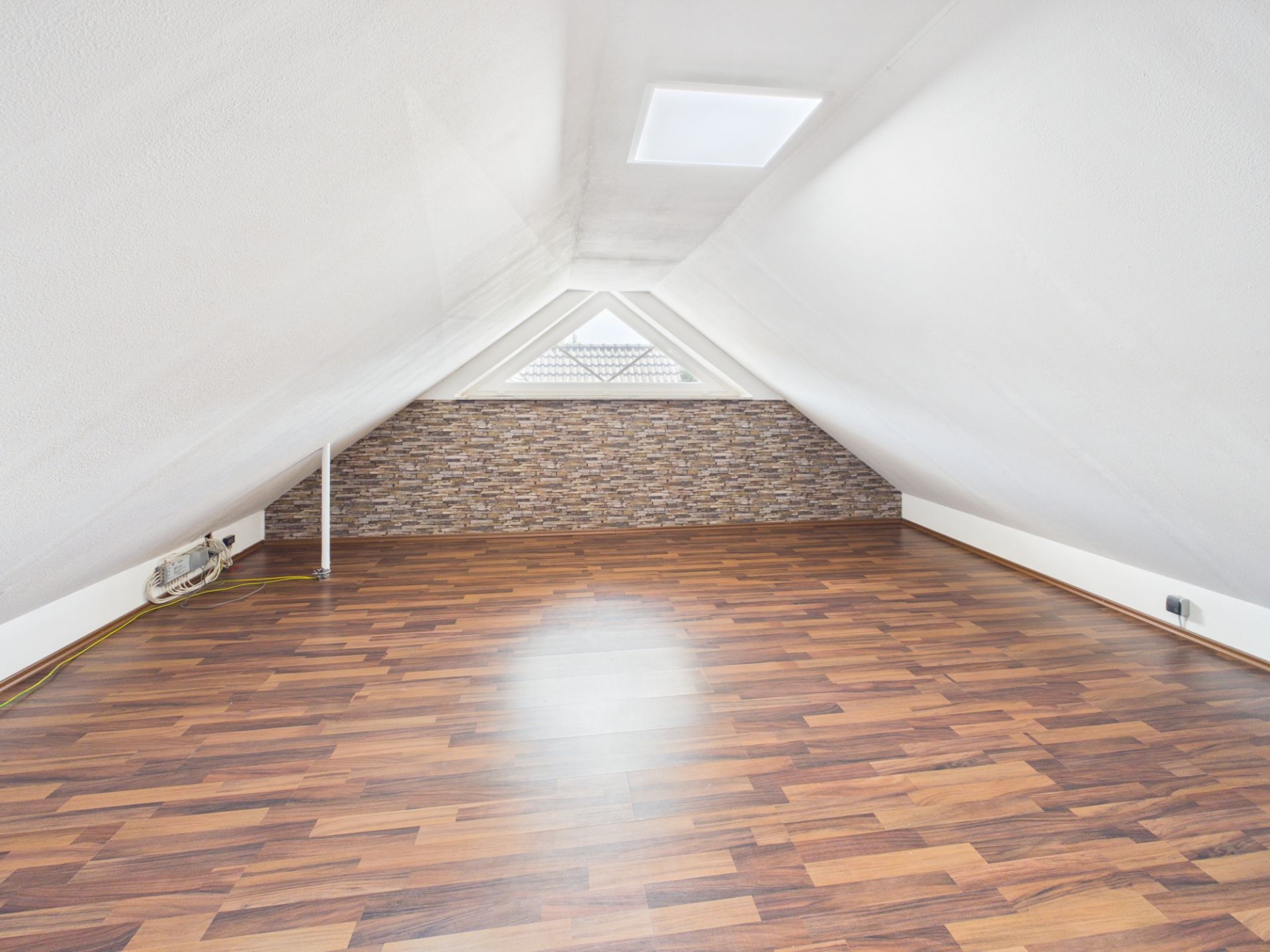 Dachbodenraum mit schrägen weißen Wänden, Fenster und Laminatboden.